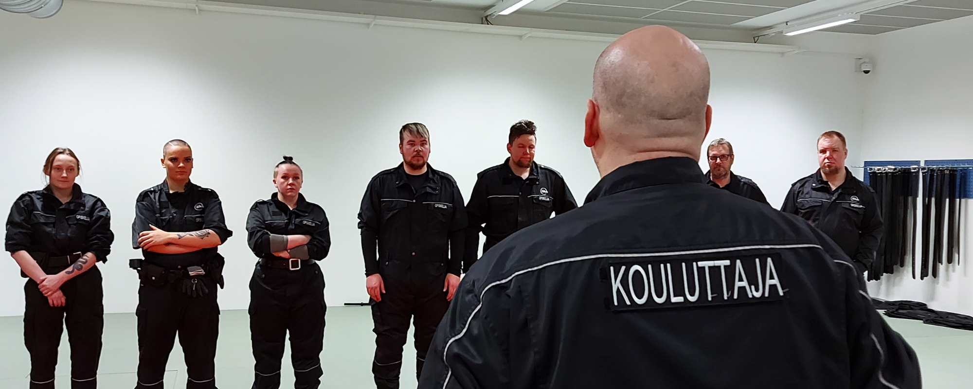 Turvallisuusalan opiskelijoita ja opettaja heidän edessään selkäpäin kameraan.