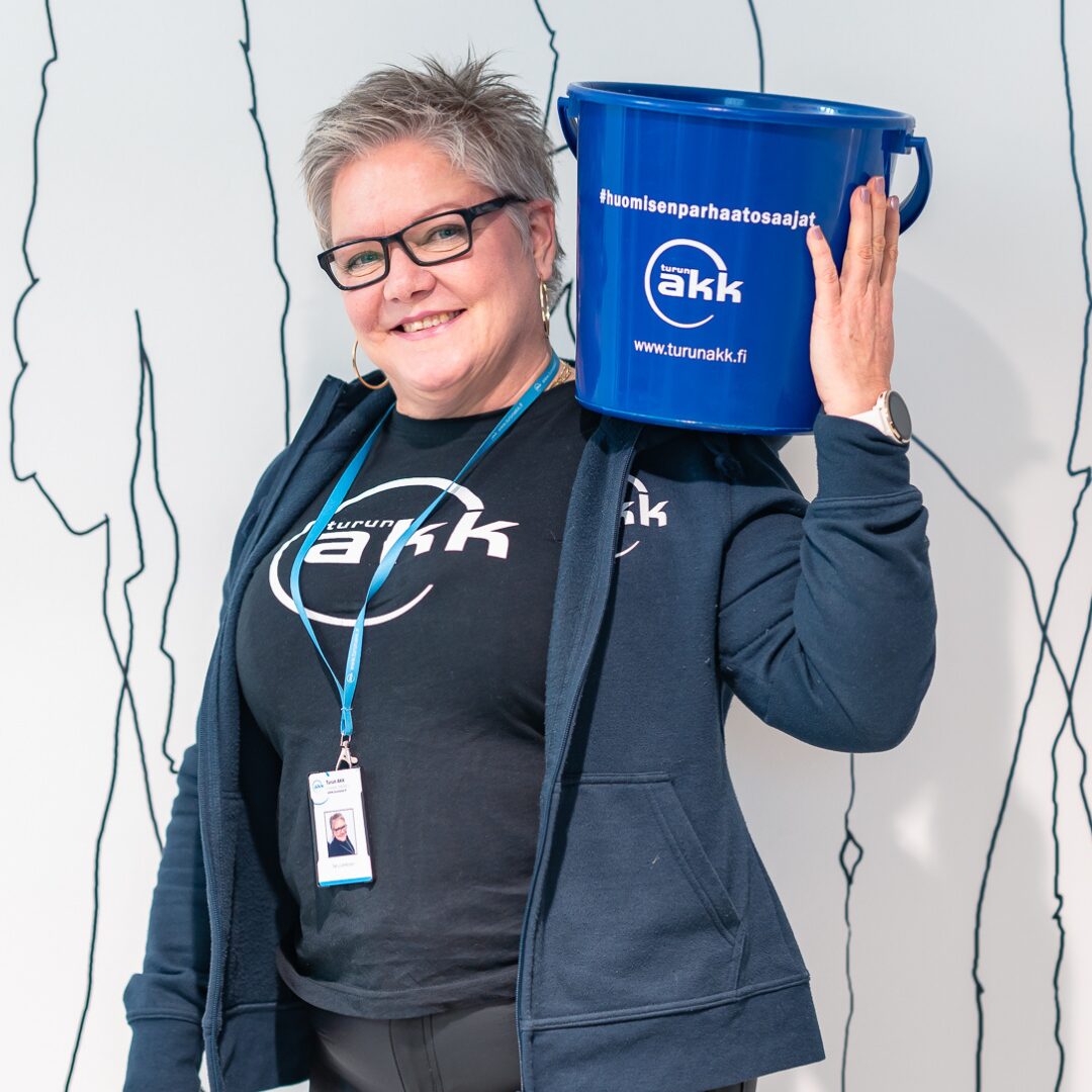 Henkilö katsoo kameraan. Hänellä on päällään Turun AKK:n T-paita ja olalla AKK:n ämpäri.