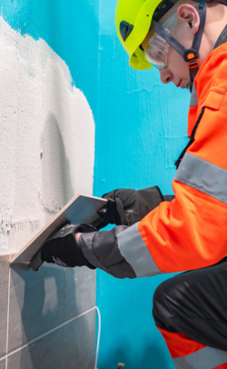 Opiskelija kiinnittää laattoja seinään kylpyhuoneremontoija-koulutuksessa.