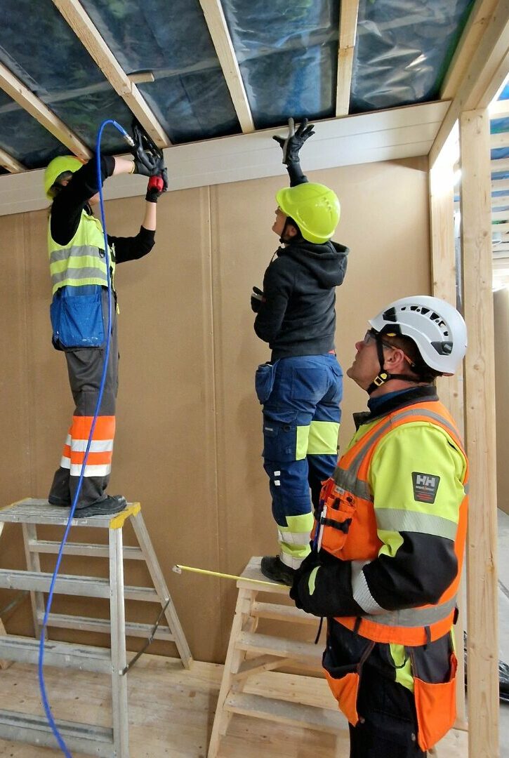 Huoneistoremontoija-opiskelijat tekemässä seinäharjoitusta ja opettaja ohjaamassa.
