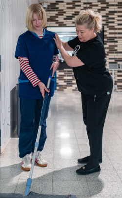 Työpaikkaohjaaja ohjaa opiskelijaa oikeaoppiseen siivousasentoon.